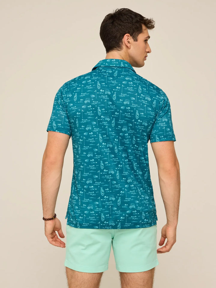 A man faces away from the camera, wearing a teal Zertz THE FAIRWAGER PERFORMANCE POLO with a white graphic pattern and light mint green shorts, set against a plain background.