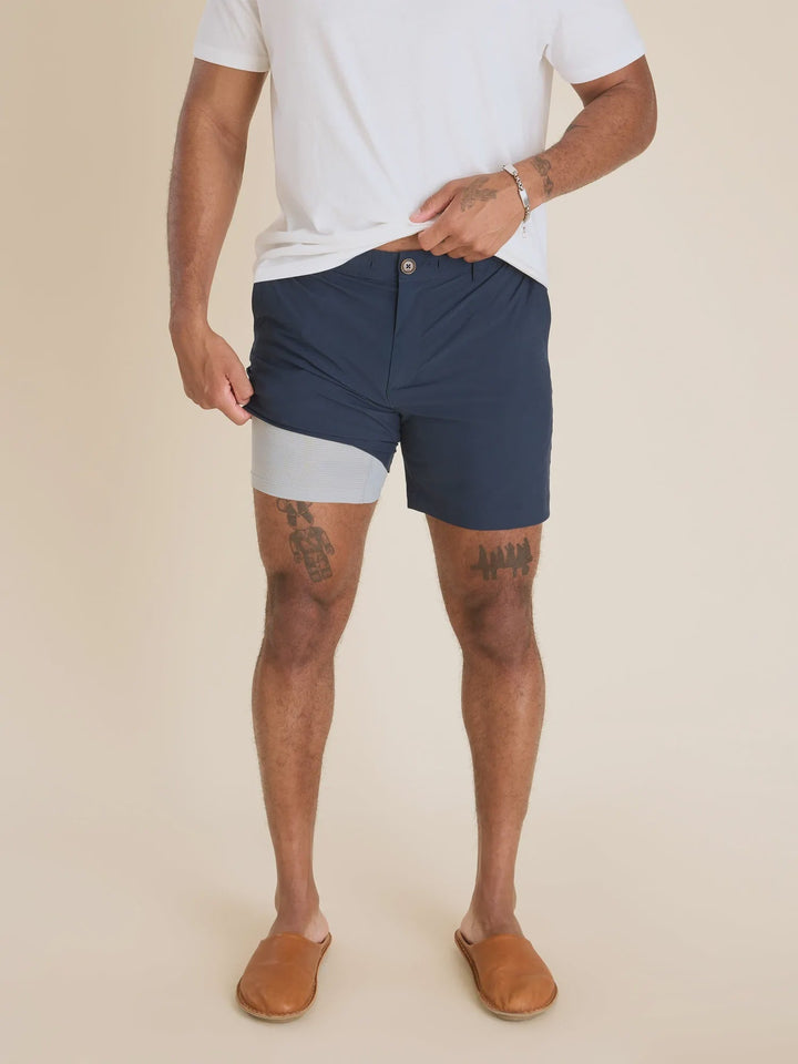 Against a beige background, a person wears a white t-shirt, brown slip-ons, and Zertz THE NAVY BABY 6&