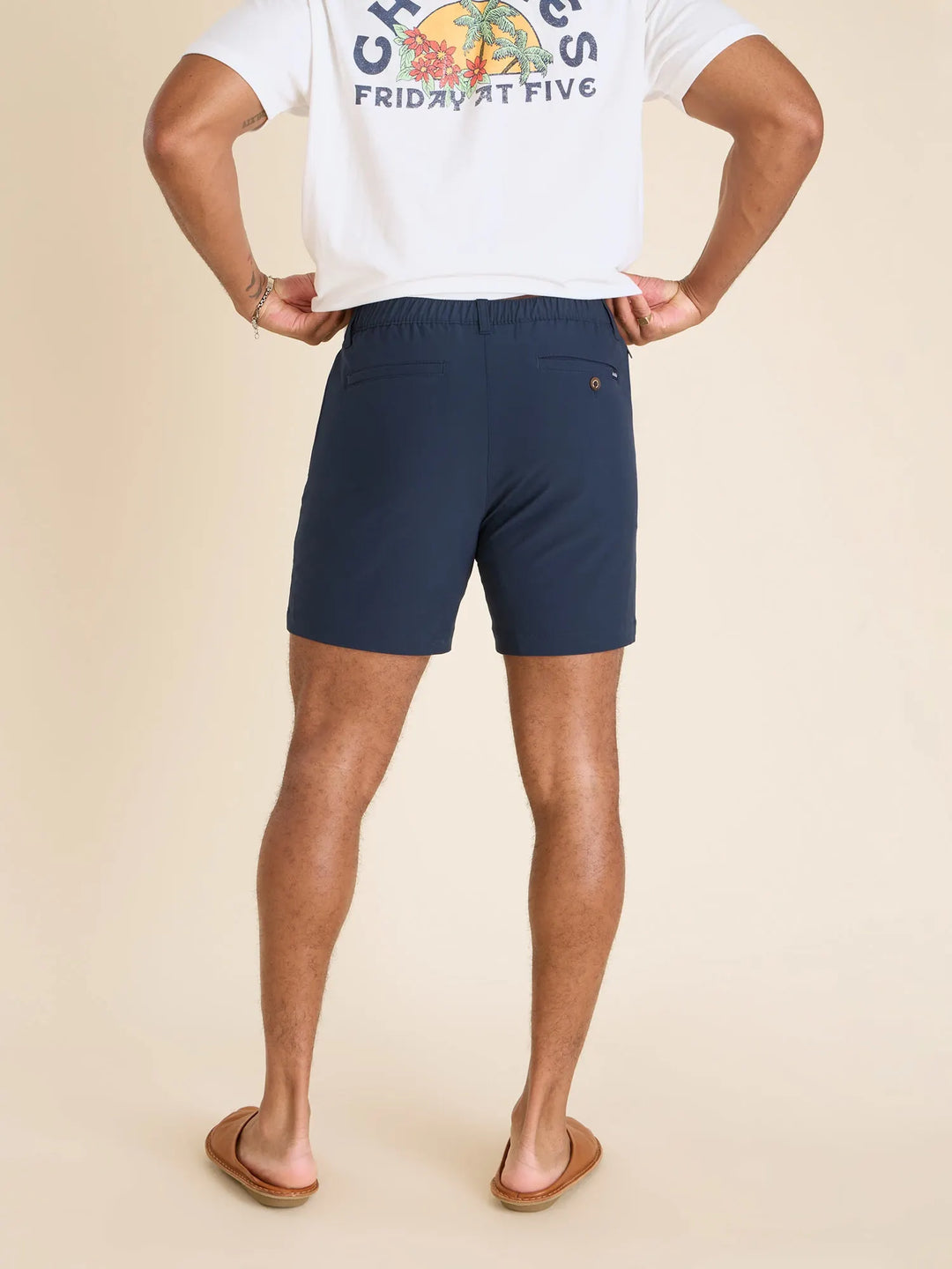 A person stands facing away against a beige background, wearing a white graphic tee, brown sandals, and Zertz THE NAVY BABY 6&