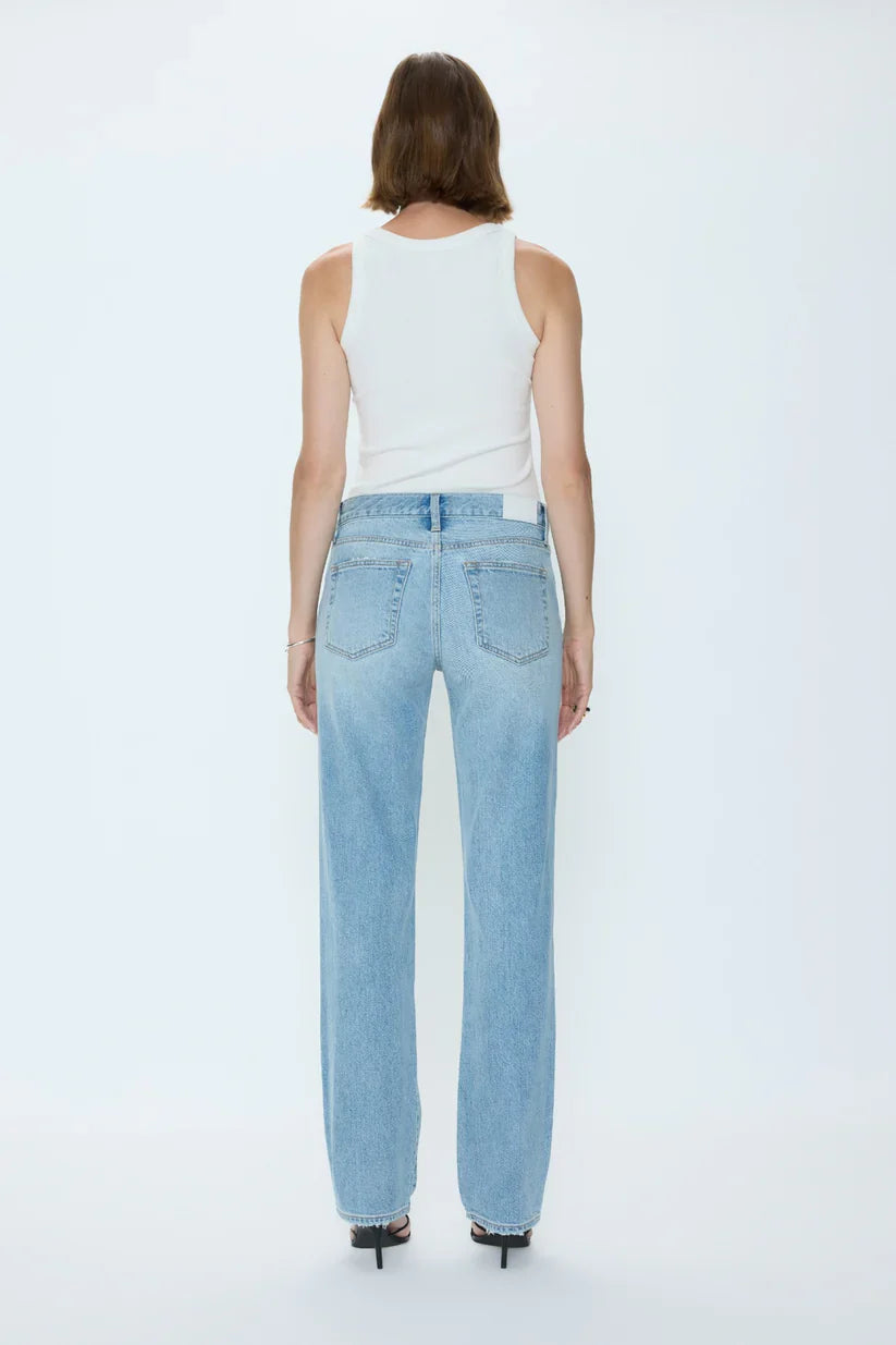 A person with shoulder-length brown hair, in a white sleeveless top, Zertz ISSA MID RISE RELAXED STRAIGHT jeans, and black heeled sandals stands facing away against a plain white background.