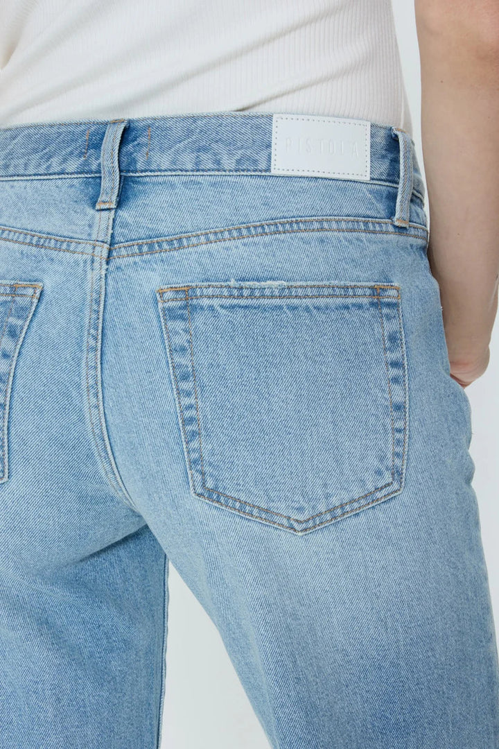 Close-up of a person wearing Zertz ISSA MID RISE RELAXED STRAIGHT jeans in light blue rigid denim, paired with a white top, highlighting the back pocket and waistband featuring a white Zertz label.
