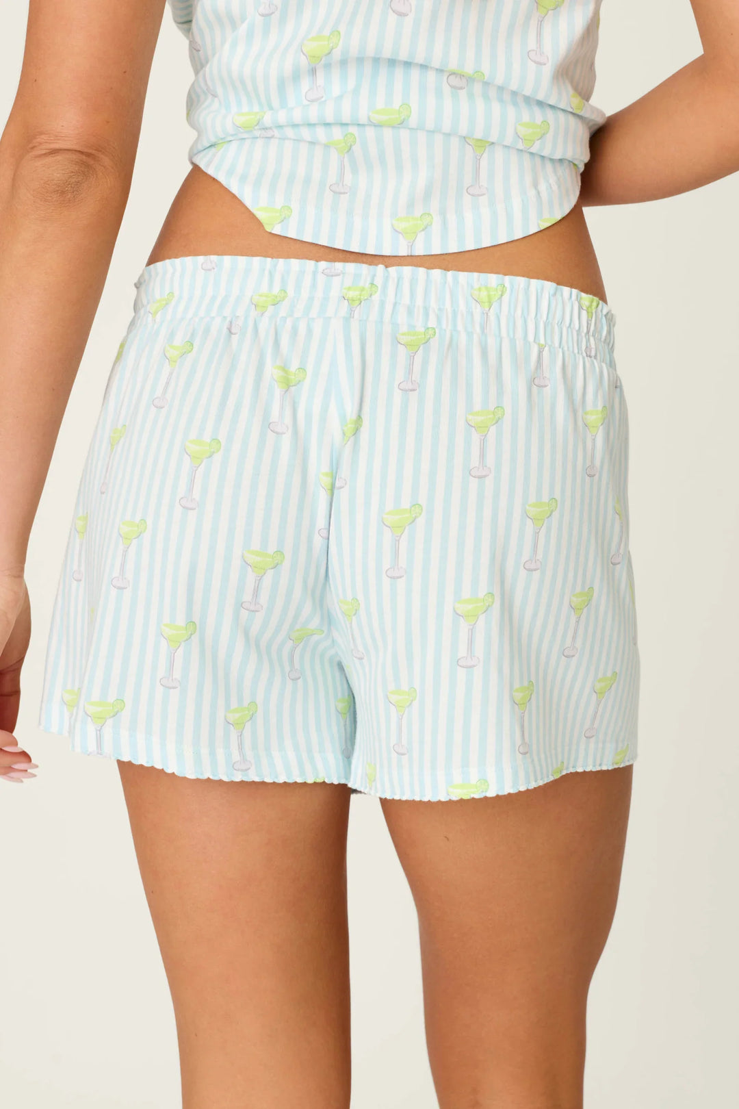 A person shown from the back wears Zertz PLAYFUL PRINTS SALTY CADILLAC PJ SHORTS in light blue and white striped cotton-modal jersey with a margarita glass pattern; their matching pajama top is partially visible.