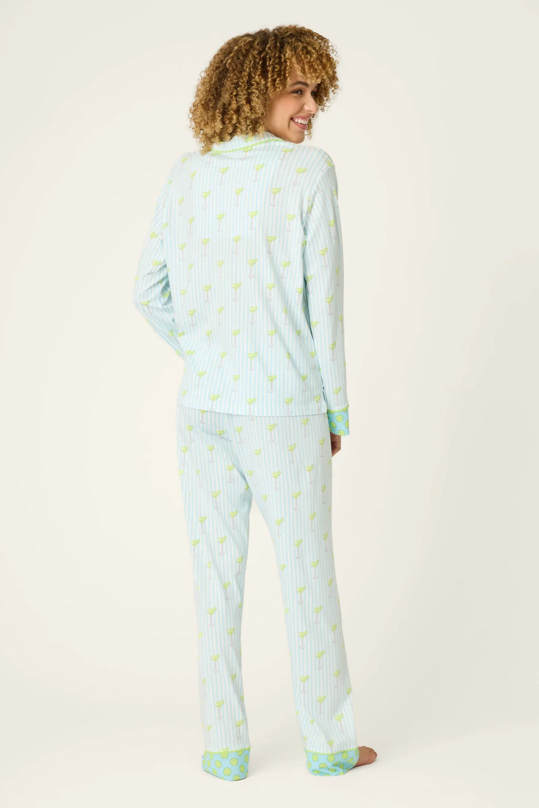 A smiling person with curly hair wears the Zertz SALTY CADILLAC STRIPE LONG PJ SET, standing barefoot and facing away from the camera against a plain background.