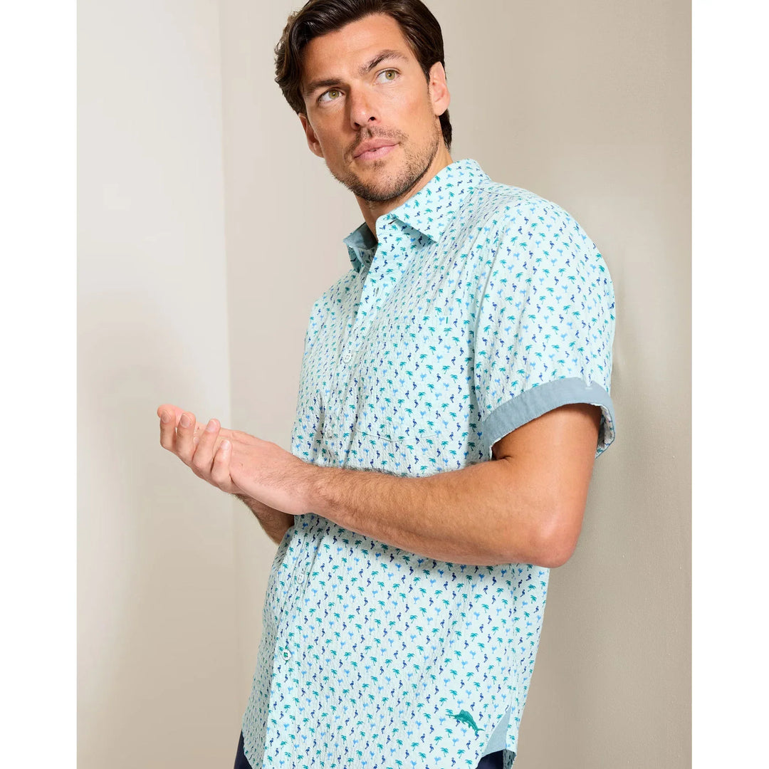 A man with short brown hair wears the Zertz NOVA WAVE FLOCK IT TO YOU light blue island-print short-sleeve shirt indoors, looking slightly left with a thoughtful expression.