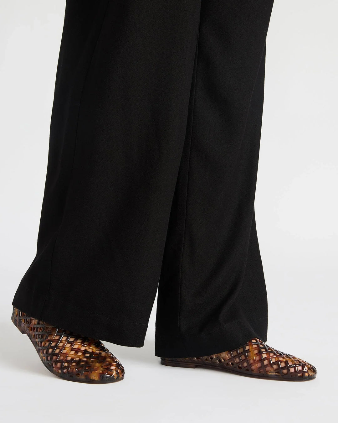 A person wears black wide-leg pants and Zertz GROVE JELLY SLIP ON brown square-toe flats with a jelly cage design, standing on a white background—ideal for comfortable everyday wear.