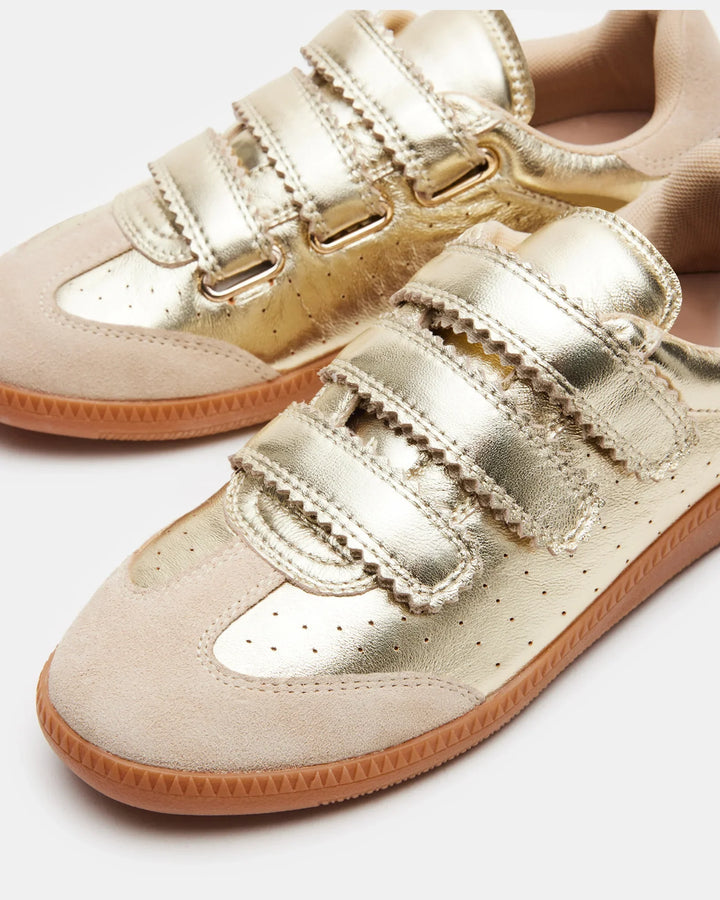 A close-up of Zertz MOMENTUM SNEAKERS in gold leather and suede with beige accents, three Velcro straps, light brown rubber soles, a metallic finish, and scalloped strap edges for decorative detail.