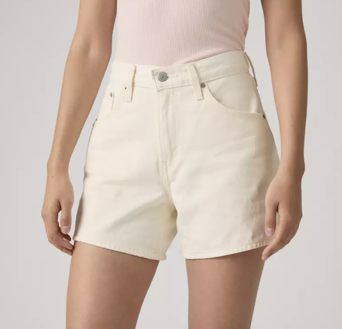 A person wearing Zertz CINCH MID-THIGH SHORT - BLANK IMPACT, high rise off-white denim shorts with an adjustable waist, and a pale pink ribbed tank top, arms relaxed at their sides, shown from mid-torso to mid-thigh against a plain background.