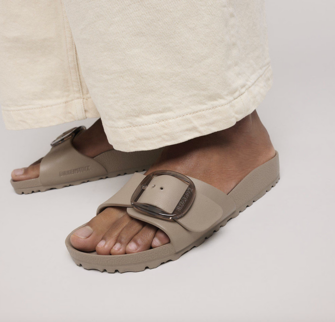 Close-up of a person in light beige wide-leg pants wearing Zertz MADRID BIG BUCKLE EVA GRAY TAUPE N slip-on sandals, standing on a light surface.