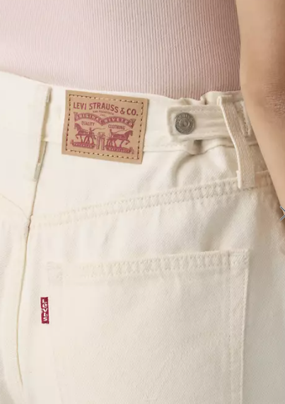 Close-up of someone wearing off-white Zertz CINCH MID-THIGH SHORT - BLANK IMPACT with a visible branded patch and back pocket tag, paired with a light pink ribbed top for a casual, stylish look.