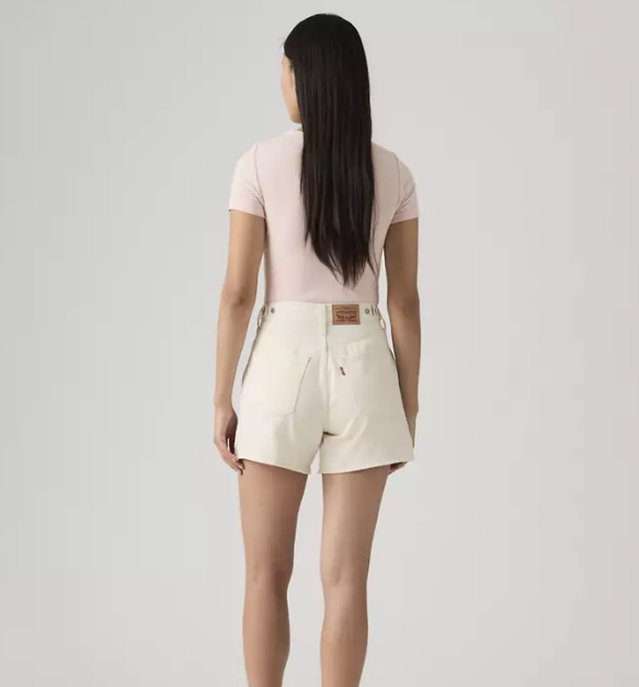A person with long dark hair, wearing a light pink short-sleeve shirt and Zertz CINCH MID-THIGH SHORT - BLANK IMPACT, stands facing away against a plain light background.