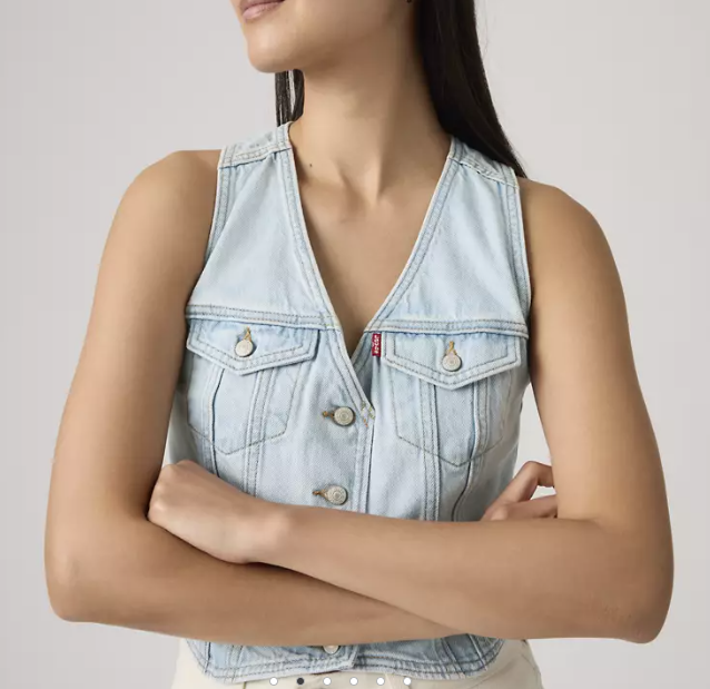 A woman with long dark hair stands with arms crossed, wearing a light blue Zertz RACER VEST - NEVER GOING TO CHANGE made from 100% cotton, featuring buttoned chest pockets, against a plain background.
