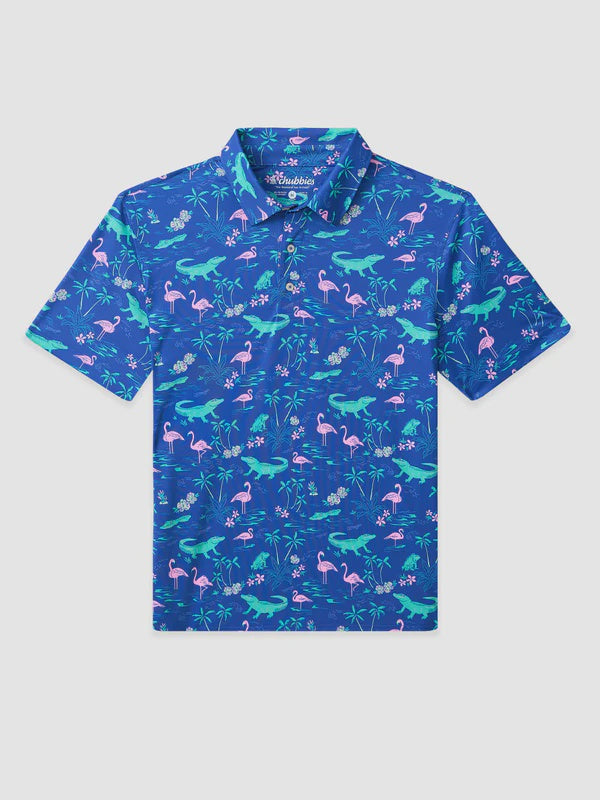 The Zertz THE LIL SWAMP&CIRCUMSTANCE BOYS PERFORMANCE POLO is a blue, short-sleeve polo with a colorful print of green alligators, pink flamingos, and tropical leaves, crafted from moisture-wicking fabric for comfort.