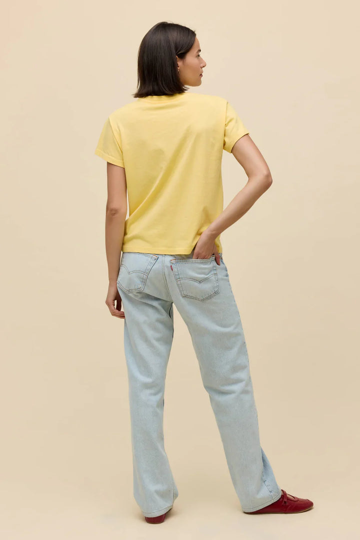 A person with short brown hair, wearing the Zertz ROLLING STONES SATISFACTION DOODLES SOLO TEE, light blue jeans, and red shoes stands facing away with one hand in their back pocket against a plain beige background, looking satisfied.