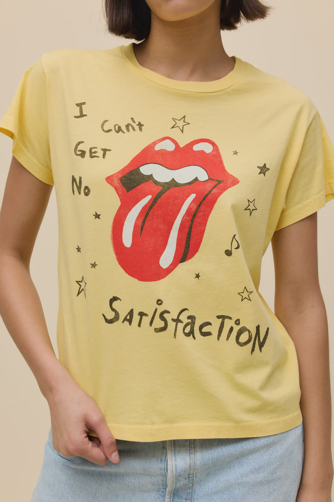 A person wearing the Zertz ROLLING STONES SATISFACTION DOODLES SOLO TEE, featuring a yellow design with a red tongue and lips graphic, stars, music notes, and the text "I can't get no satisfaction.