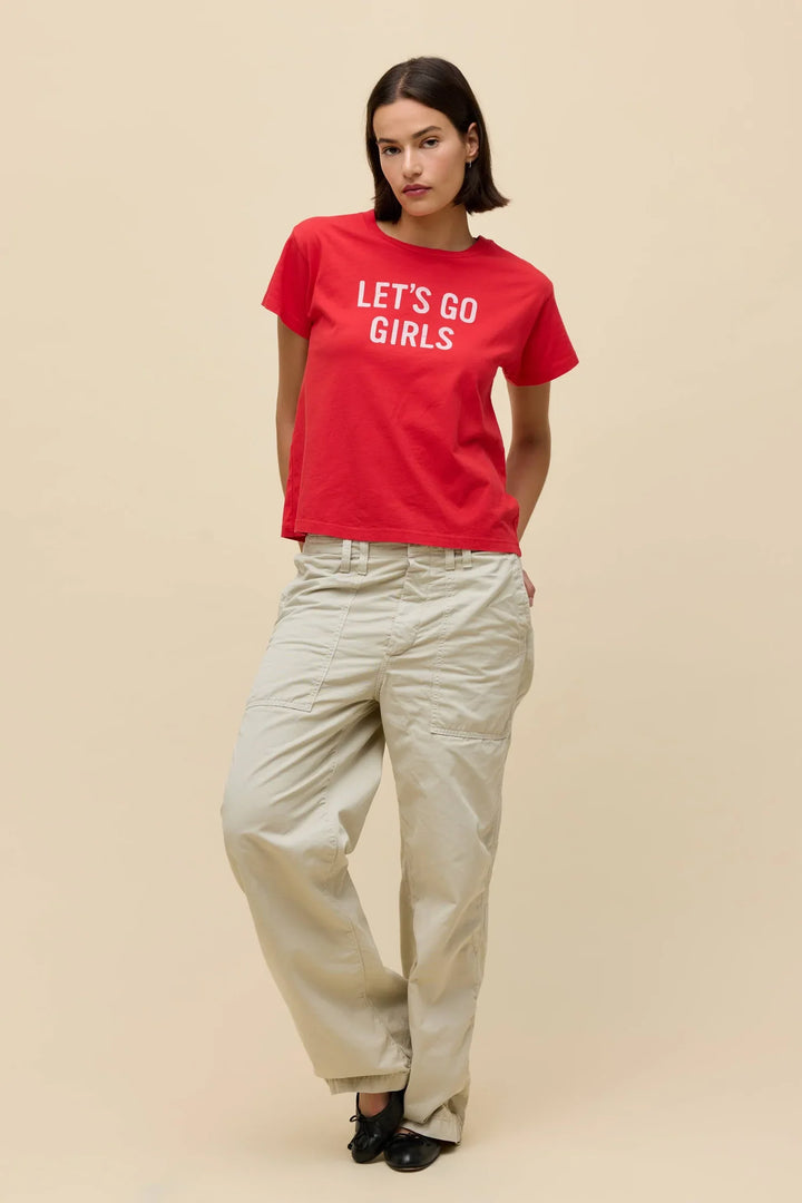 A woman stands against a beige background wearing the Zertz SHANIA TWAIN LETS GO GIRLS SOLO TEE in red, paired with light beige cargo pants and black shoes, her hands in her pockets.