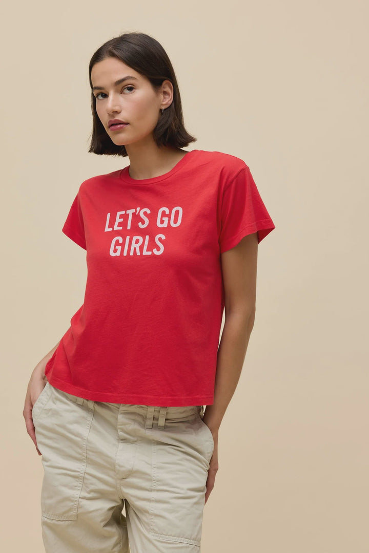 A woman with a short dark bob models the Zertz SHANIA TWAIN LETS GO GIRLS SOLO TEE, a red shirt with bold white text, paired with light beige cargo pants against a plain beige background.