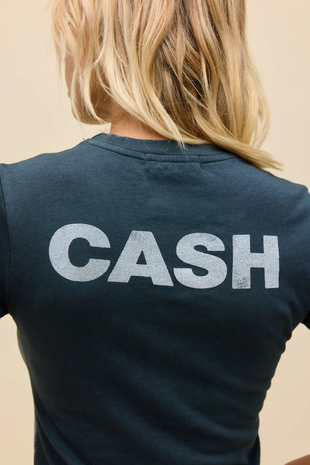 A blonde-haired person is seen from behind wearing the Zertz JOHNNY CASH SILHOUETTE VNTG TEE, a dark vintage shirt featuring bold white "CASH" lettering on the back as a tribute to Johnny Cash.