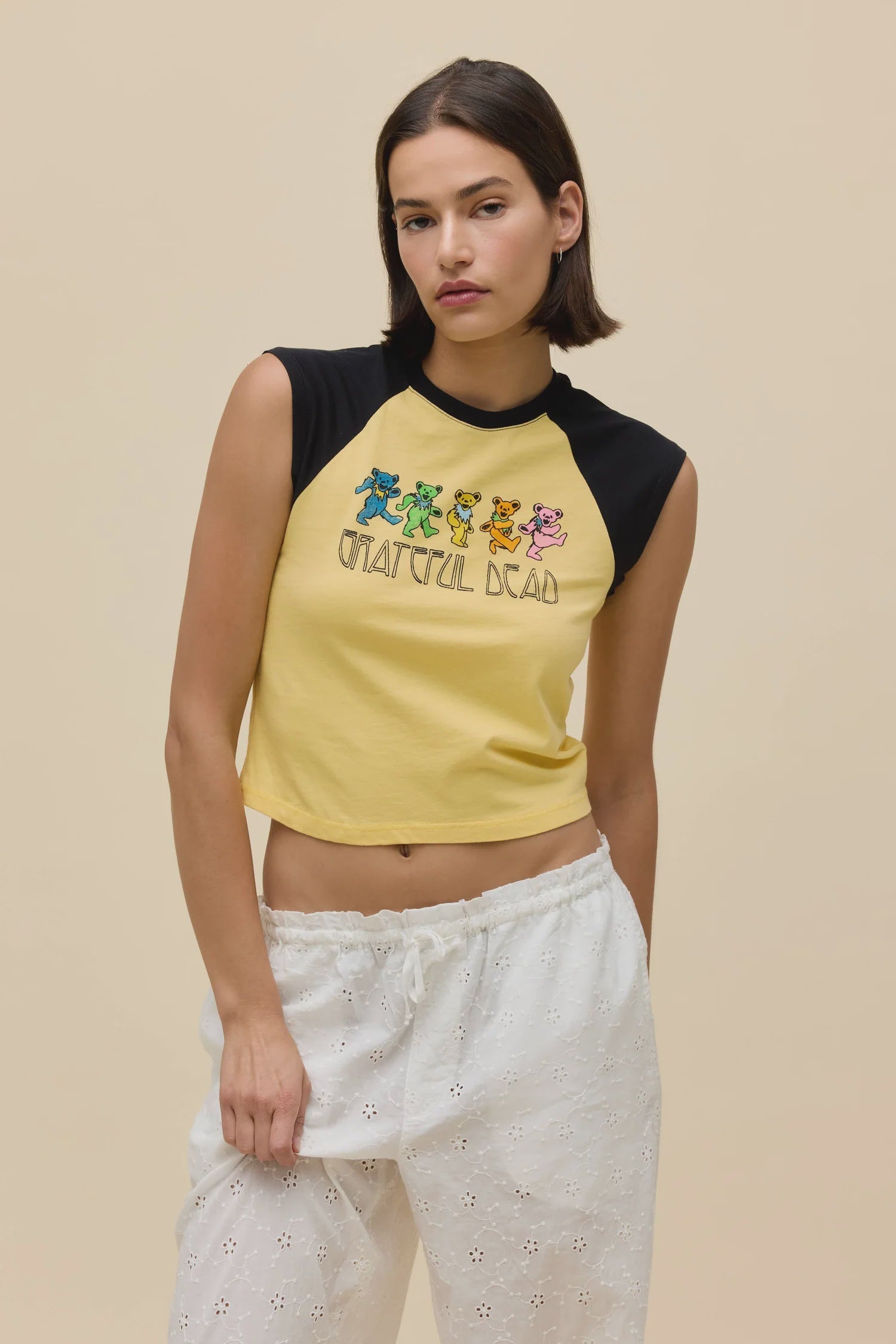 A woman with short brown hair wears the Zertz GREATFUL DEAD BEARS RGLAN TEE with dancing bears, paired with white eyelet pants, standing against a plain beige background.