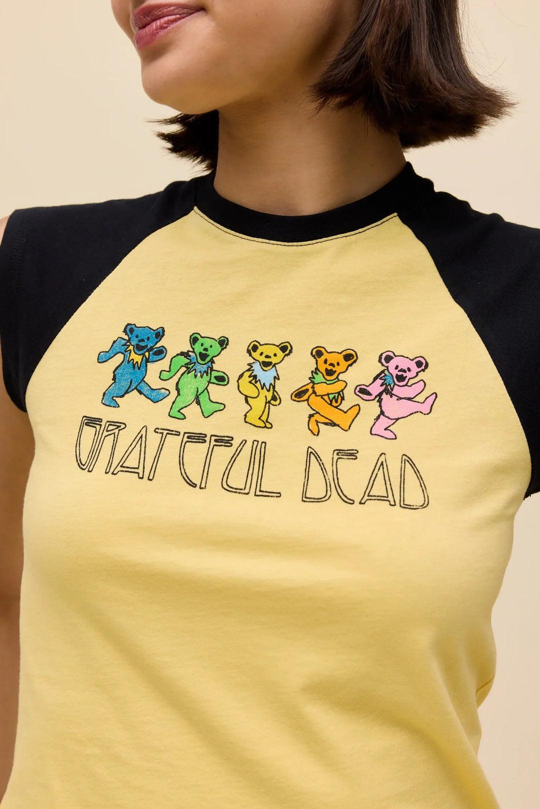 A person wearing a Zertz GREATFUL DEAD BEARS RGLAN TEE, a yellow and black raglan top featuring five colorful dancing bears and “Grateful Dead” text on the front.
