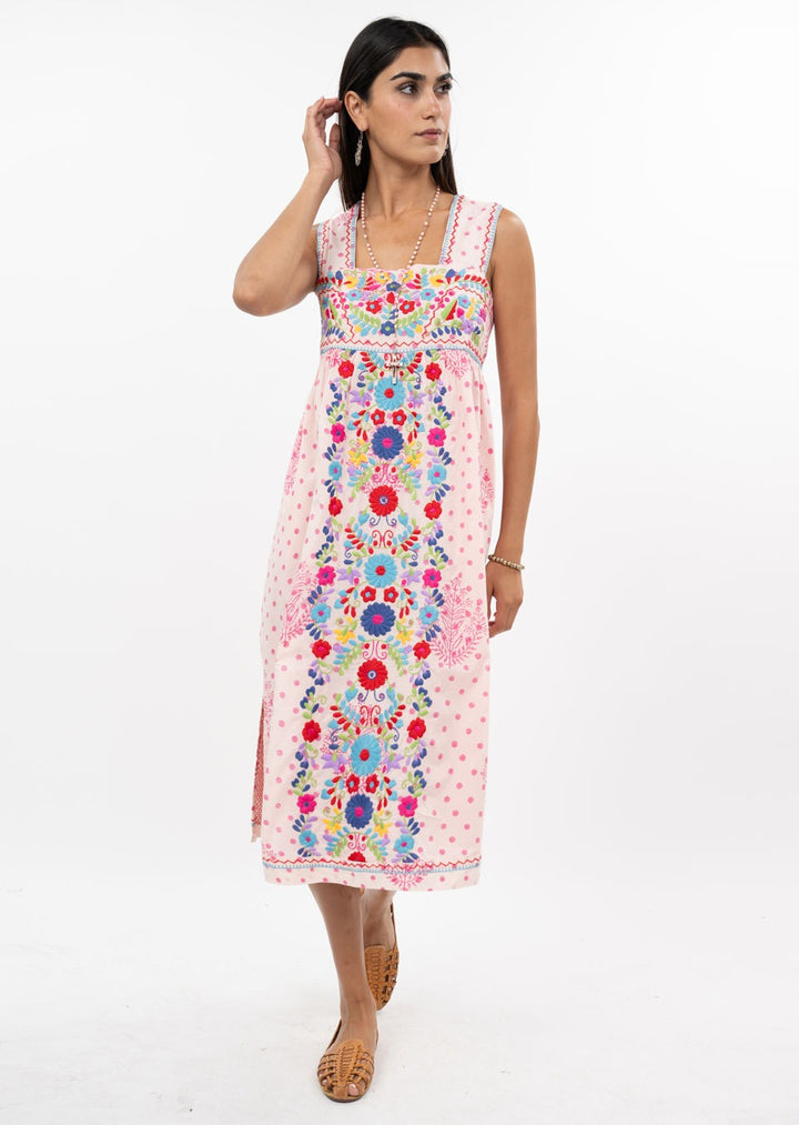 A woman poses against a white background wearing the Zertz VALNTINA EMBD FLOWER MIDI DRESS, a pink sleeveless dress with colorful floral embroidery, paired with tan woven shoes and jewelry—ideal for special occasions.
