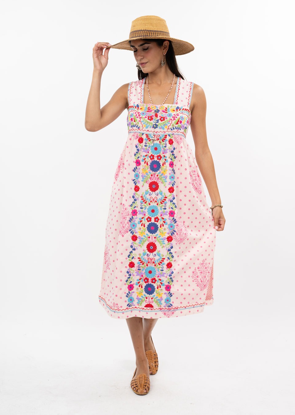 A woman models the Zertz VALNTINA EMBD FLOWER MIDI DRESS—a pink midi dress with colorful floral embroidery—paired with a straw hat and woven brown flats, standing against a white background.