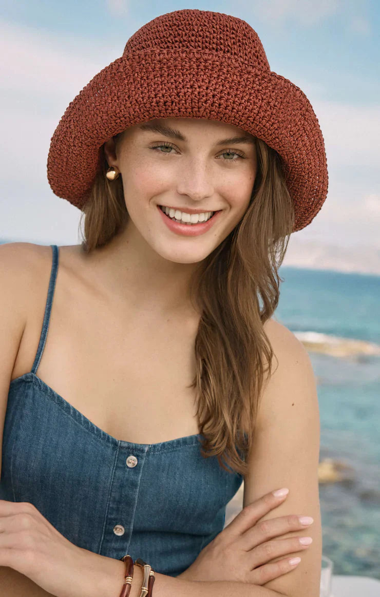A woman wearing the Zertz ANGEL EYES DENIM MINI DRESS in medium indigo stands outdoors by the sea, arms crossed and smiling at the camera, with a blue sky behind her.