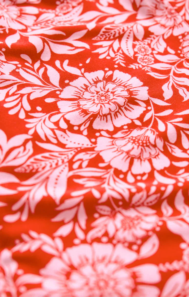 Close-up of the Zertz CHARISMA ONA FLORAL MIDI DRESS: red fabric with white floral and leafy patterns. Large flowers pop for a summery look, while gentle wrinkles add textured detail to this striking botanical design.