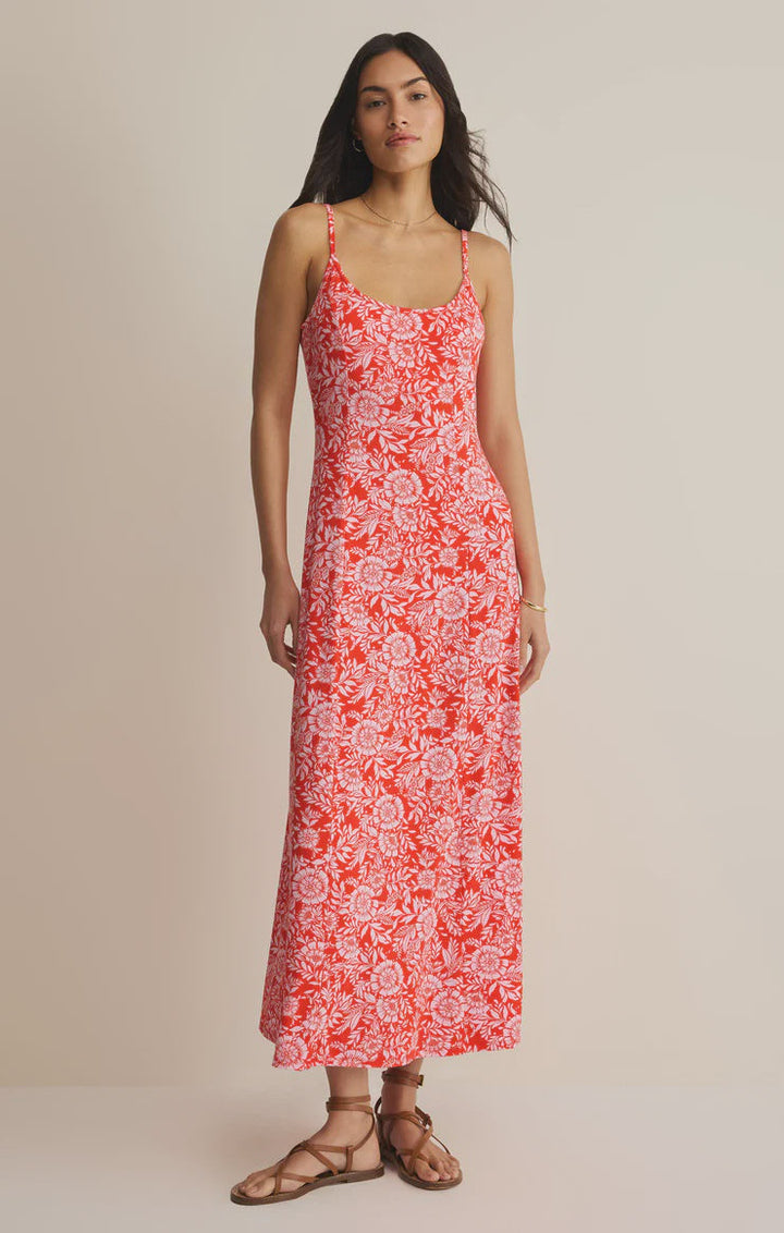 A woman stands against a plain background wearing the Zertz CHARISMA ONA FLORAL MIDI DRESS, a sleeveless, ankle-length floral dress with adjustable spaghetti straps, paired with brown flat sandals.