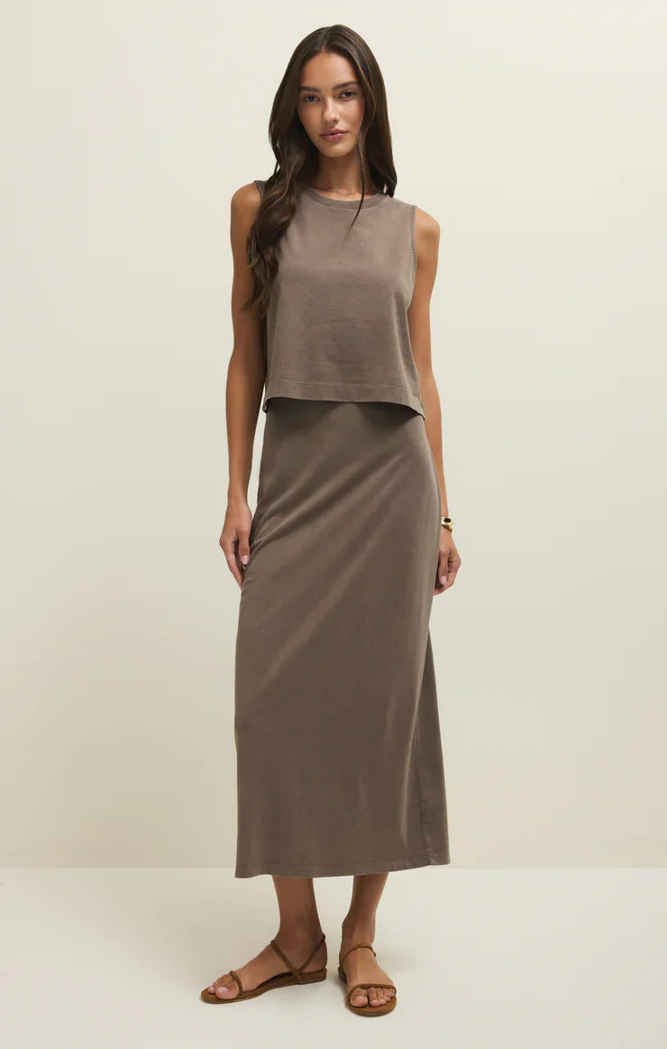 A woman stands against a plain background, wearing the Zertz GAIL MIDI SKIRT PERFECTLY TAUPE, styled with a matching sleeveless crop top, flat brown sandals, a gold bracelet, and her long hair loose.