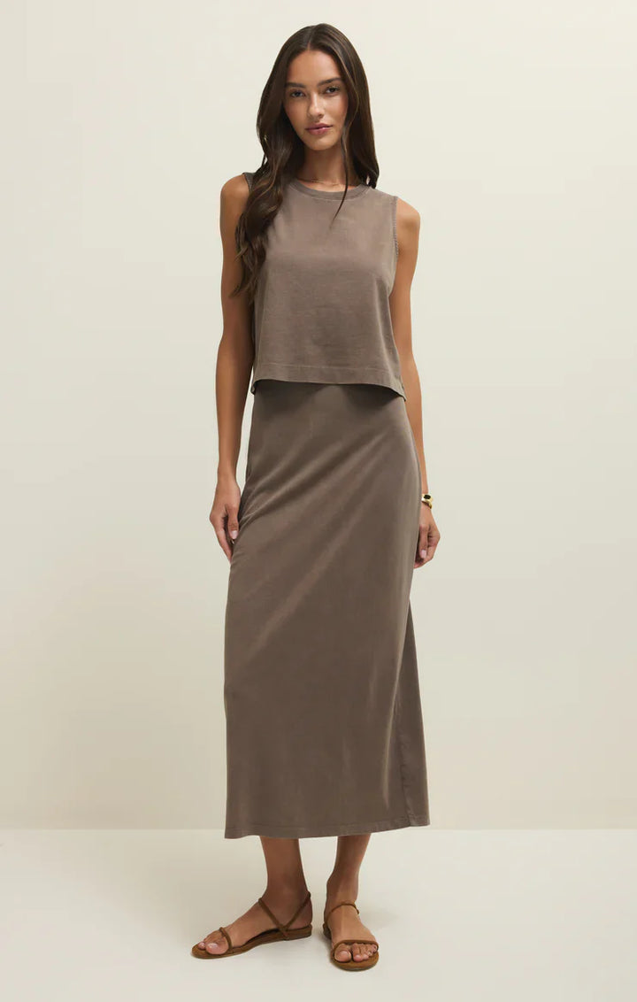 A woman stands against a plain background, wearing the Zertz GAIL MIDI SKIRT PERFECTLY TAUPE, styled with a matching sleeveless crop top, flat brown sandals, a gold bracelet, and her long hair loose.