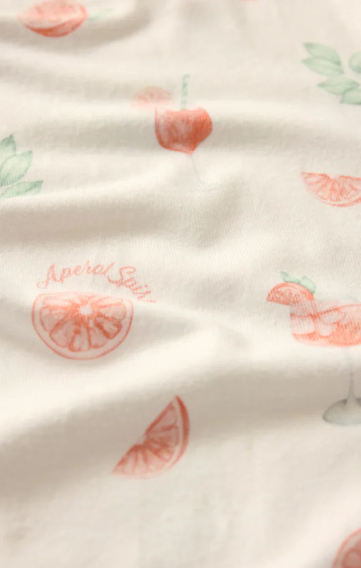 A close-up of Zertz's APEROL SPRITZ SHORT shows white pj shorts with pink grapefruit slices, red cherries, green leaves, and a pink Aperol Spritz drink. The high-waisted style features soft folds and a smooth finish.