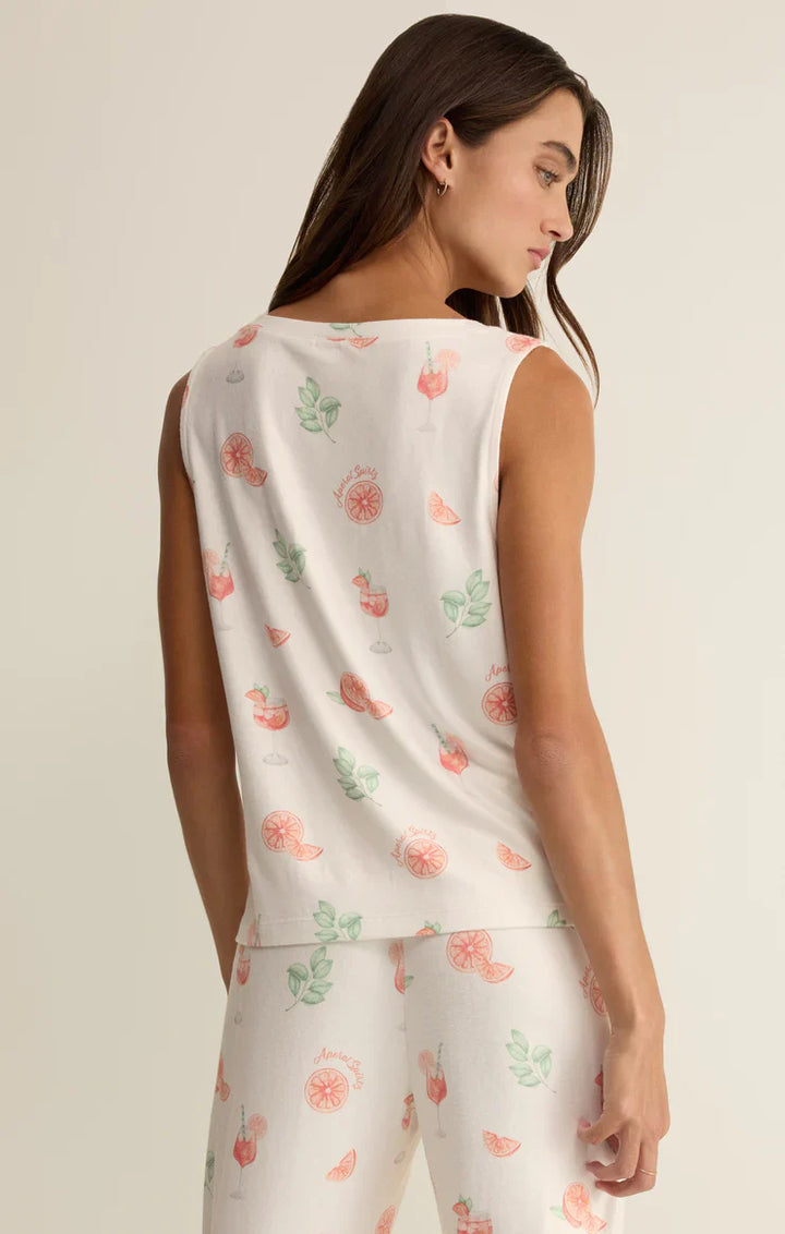 A woman with long brown hair models the Zertz SPRITZ TANK—a lightweight v-neck top with matching bottoms featuring a vibrant fruit and leaf print—as she looks over her shoulder against a neutral background.