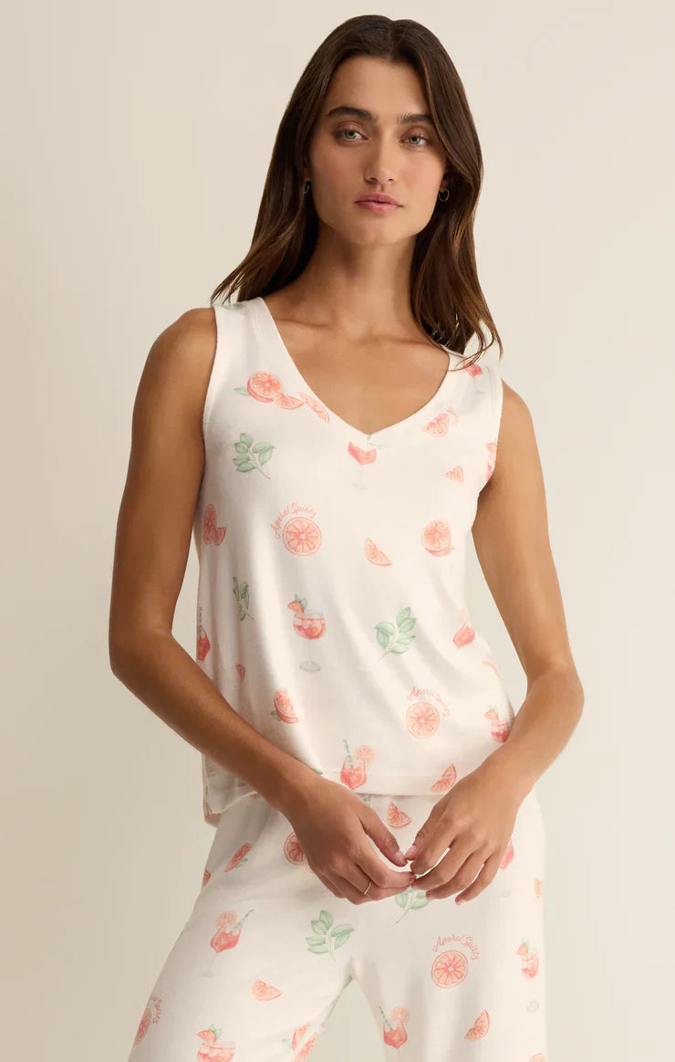 A woman wears the Zertz SPRITZ TANK, a white sleeveless pajama top featuring a lightweight v-neck and colorful fruit prints like oranges and strawberries. She faces the camera with a neutral expression.