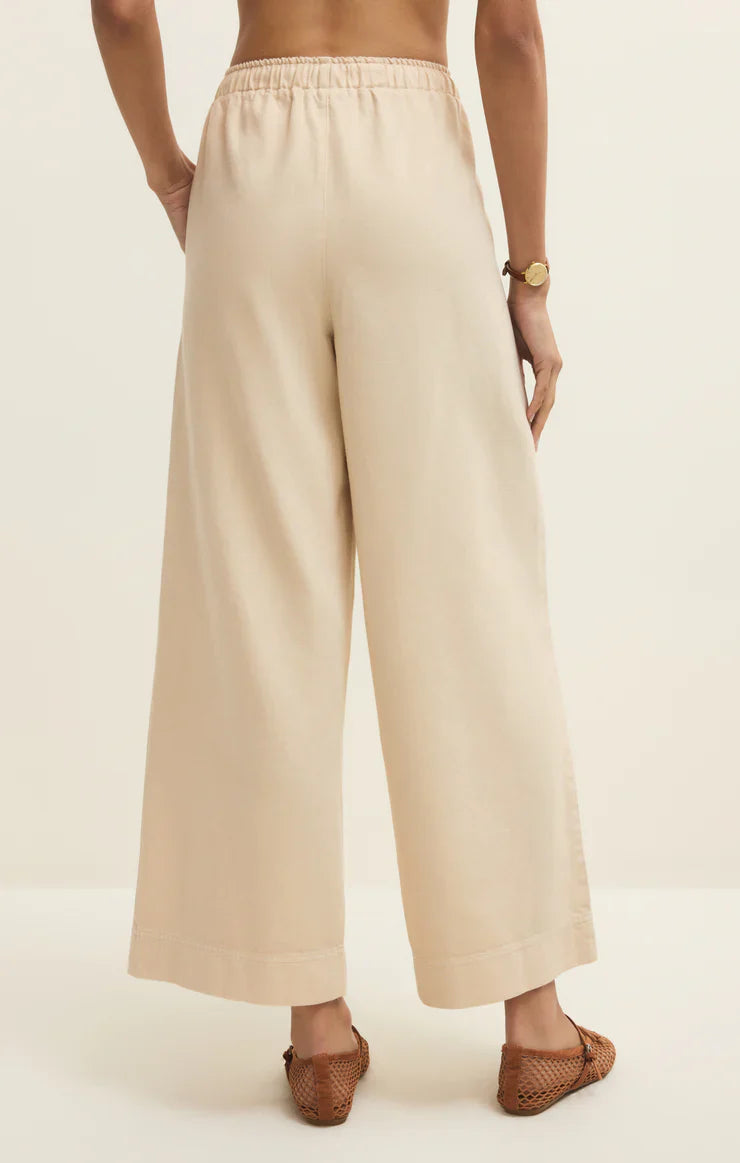 A person is seen from the back wearing Zertz DAYCATION PANT—high-waisted, wide leg with an elastic waistband—paired with brown woven flats and a watch, set against a plain light background.