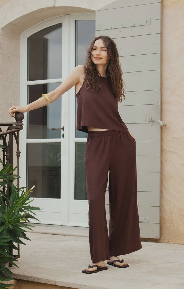 A woman with long wavy hair smiles outside by a railing, wearing Zertz&