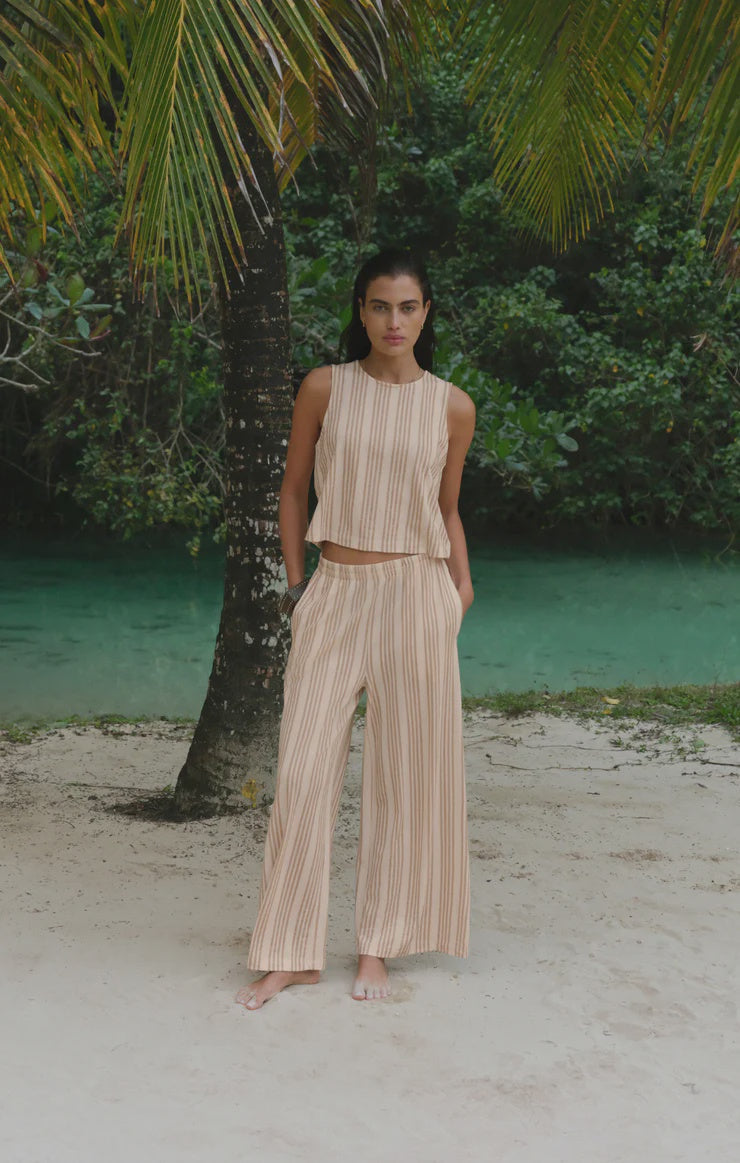 A woman stands barefoot near a palm tree, wearing Zertz&