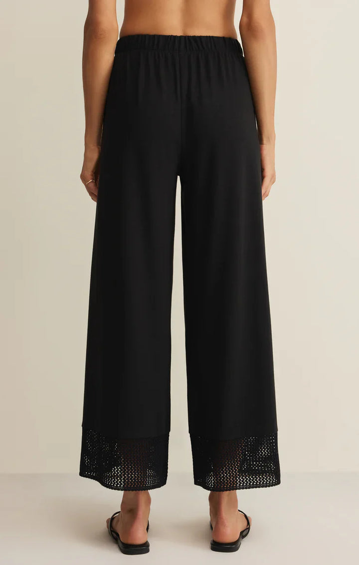 A person, barefoot and seen from the back against a plain light background, wears the Zertz BANYAN PANT—relaxed straight-leg pants featuring an elastic waistband and mesh hem detail.