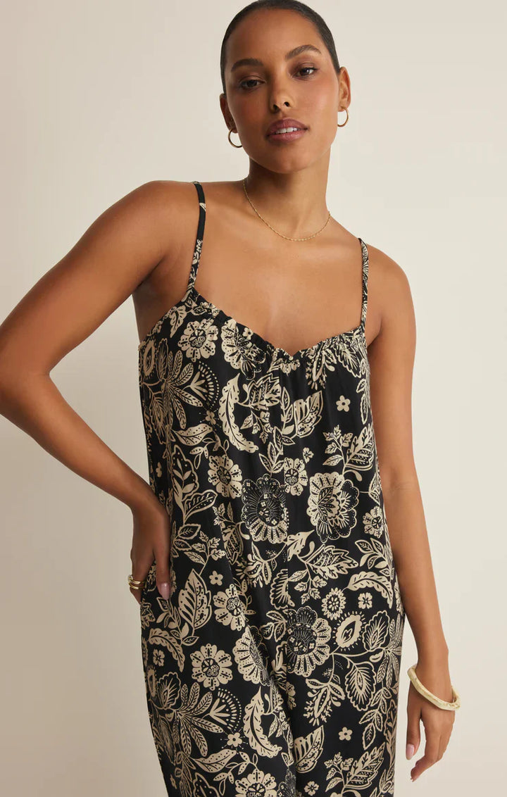 A woman with short hair models the Zertz DAY OFF LUZ FLORAL JUMPSUIT, a relaxed fit stretch jersey piece. She stands against a light background, hand on hip, accessorized with hoop earrings and bracelets.