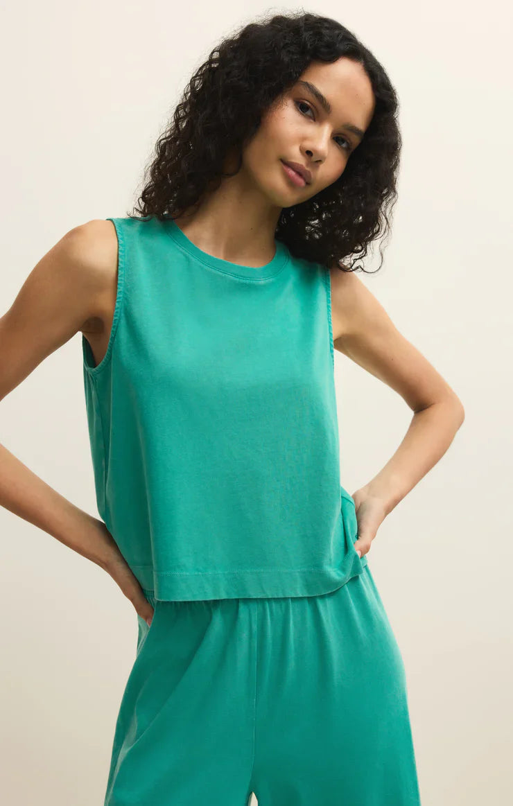 A woman with curly dark hair models the Zertz SLOANE JERSEY MUSCLE TANK and matching pants, posing against a plain light background with one hand on her hip.