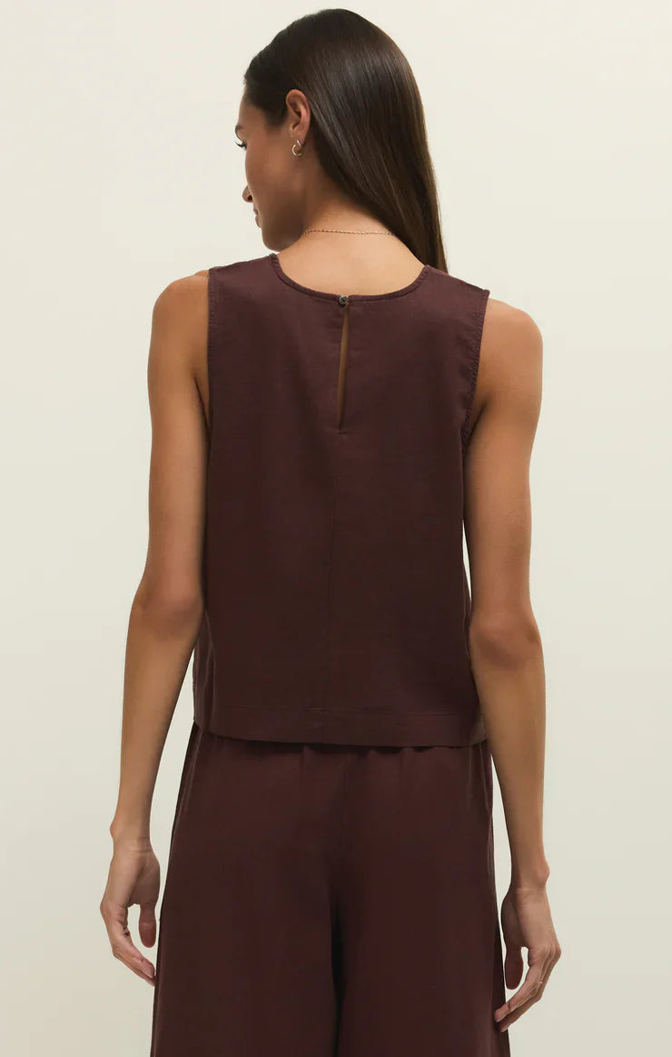 A woman with long, straight brown hair is seen from the back wearing the Zertz SLOANE LINEN TOP, a sleeveless dark brown linen blend tank with matching loose pants. The relaxed fit flatters her shape against a plain light background.