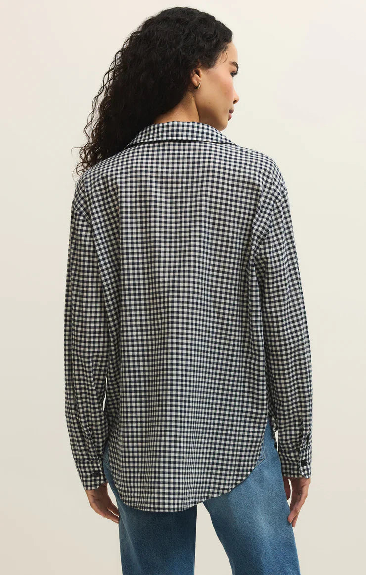 A person with long curly hair is seen from the back, wearing the Zertz SEAPORT BUTTON UP TOP in a black and white plaid print with blue jeans, set against a plain light background.