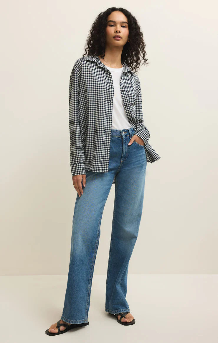 A person with curly hair wears the Zertz SEAPORT BUTTON UP TOP over a white t-shirt, paired with blue wide-leg jeans and black sandals, standing against a plain light background.