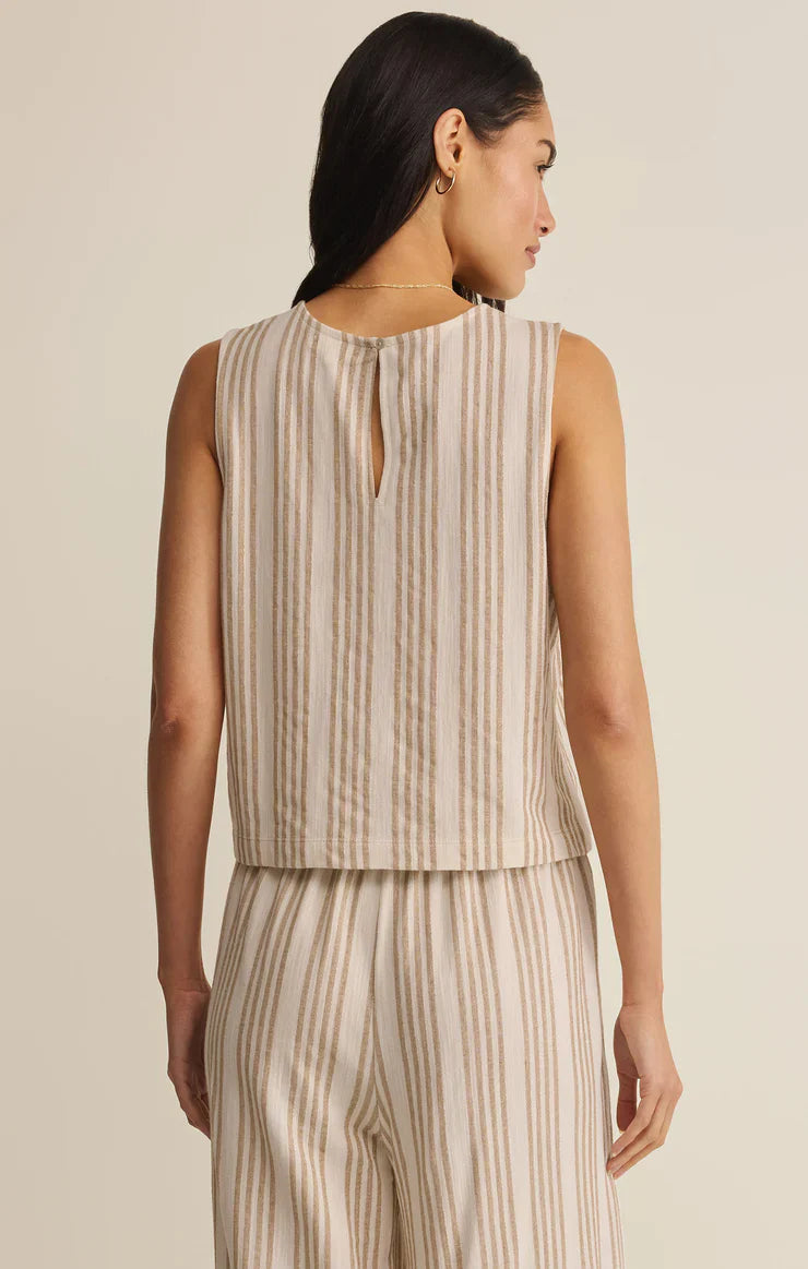 A woman faces away, wearing the Zertz SLOANE KNIT STRIPED TOP— a sleeveless, lightweight cotton blend with beige and white vertical stripes and a small keyhole at the back— set against a plain light background.