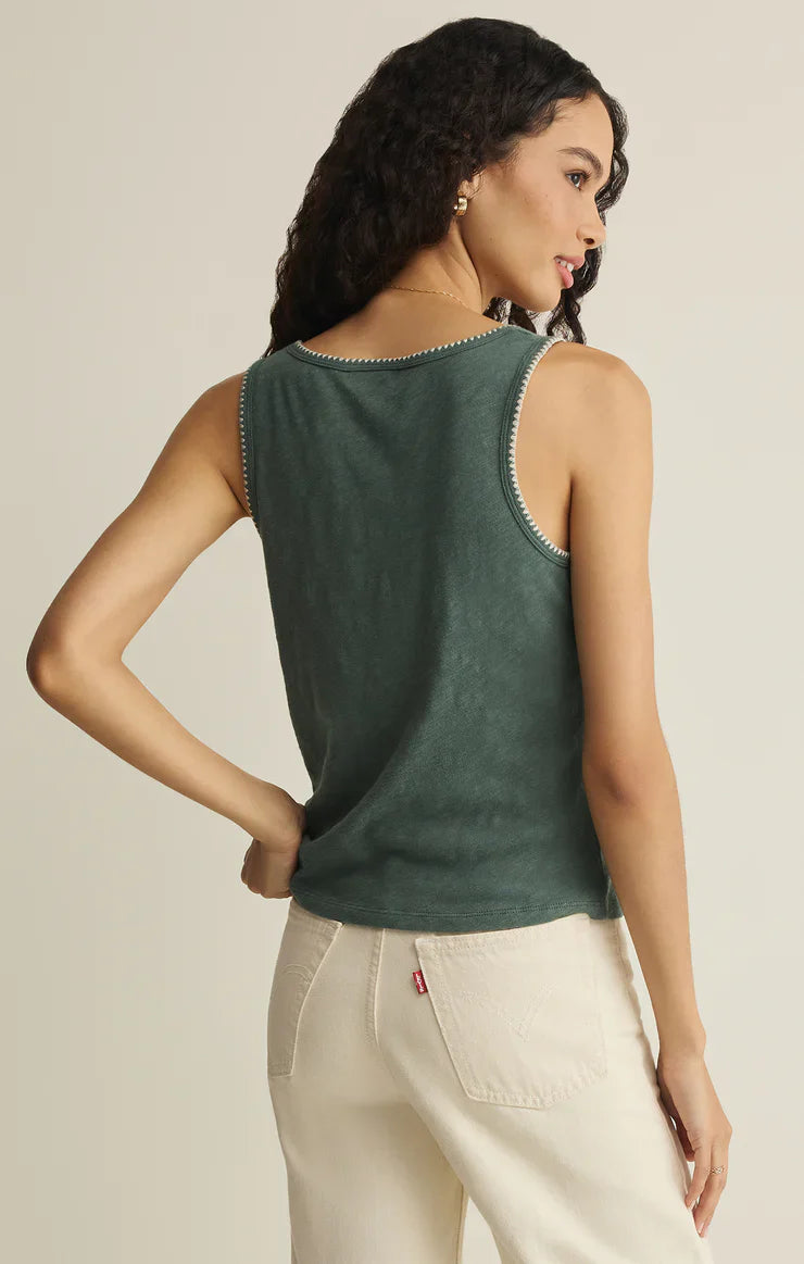 A woman with long curly hair wears the Zertz JULIAN CROCHET TANK in dark green with white stitching and off-white high-waisted jeans, standing with her back to the camera and one hand on her hip.
