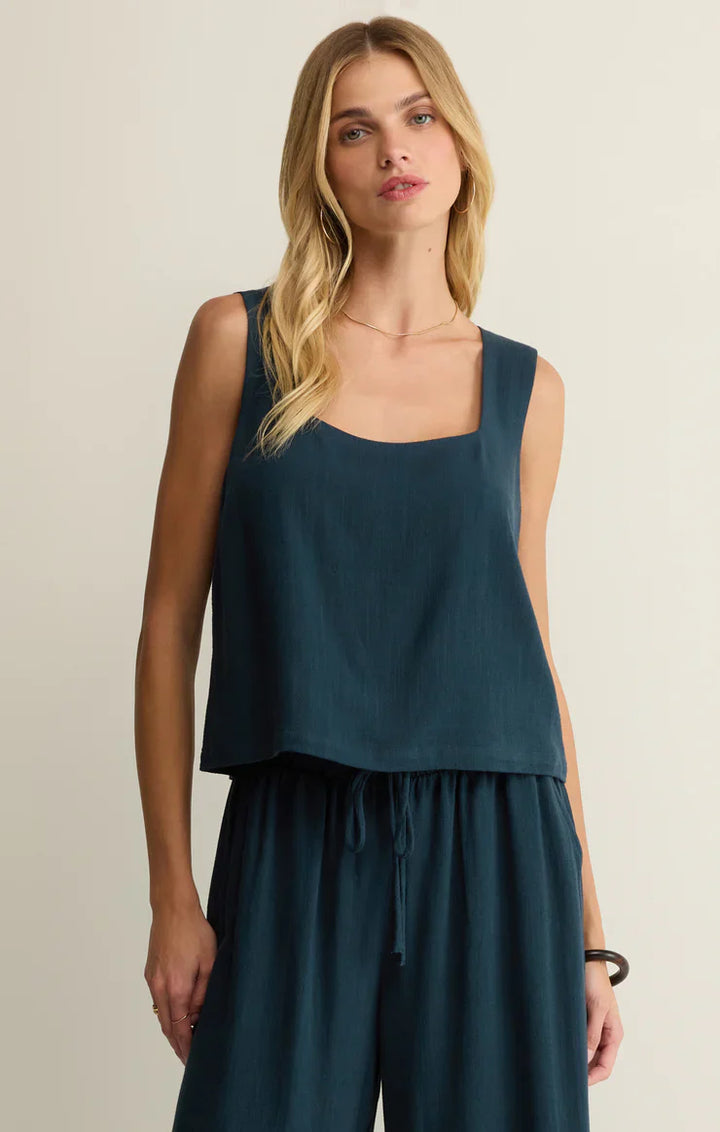 A woman with long blonde hair models the Zertz CHARLI TOP—a lightweight, sleeveless linen summer top with a cropped square neckline—paired with matching loose pants. She stands against a light background, gazing neutrally at the camera.