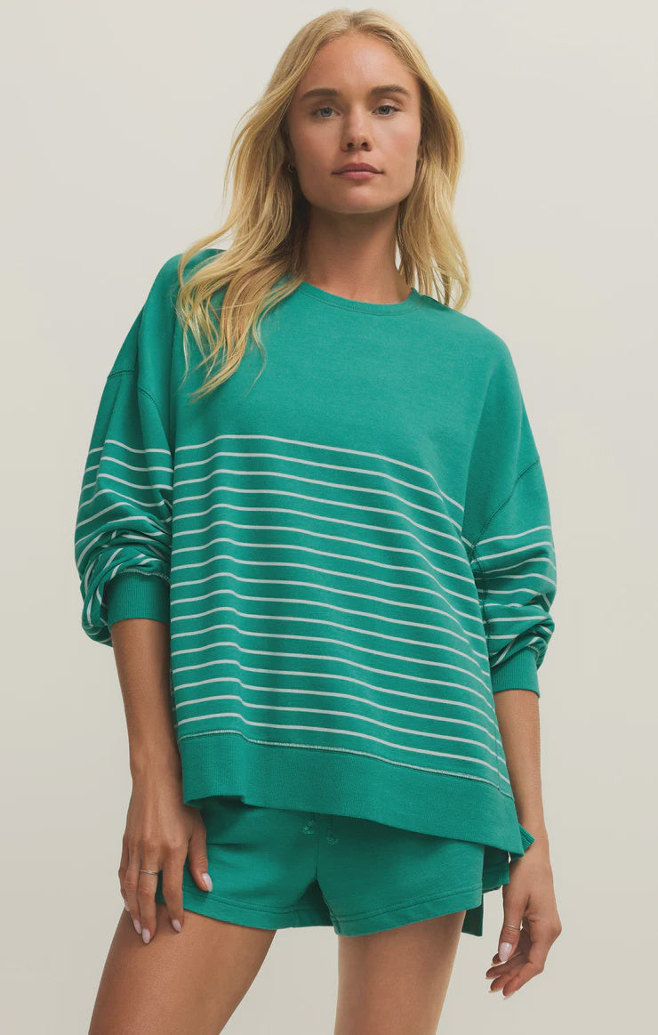 A woman with long blonde hair models the Zertz MODERN WEEKENDER STRIPE LA PALMA set— a loose green crewneck sweatshirt with white stripes and matching shorts—standing against a plain light background.