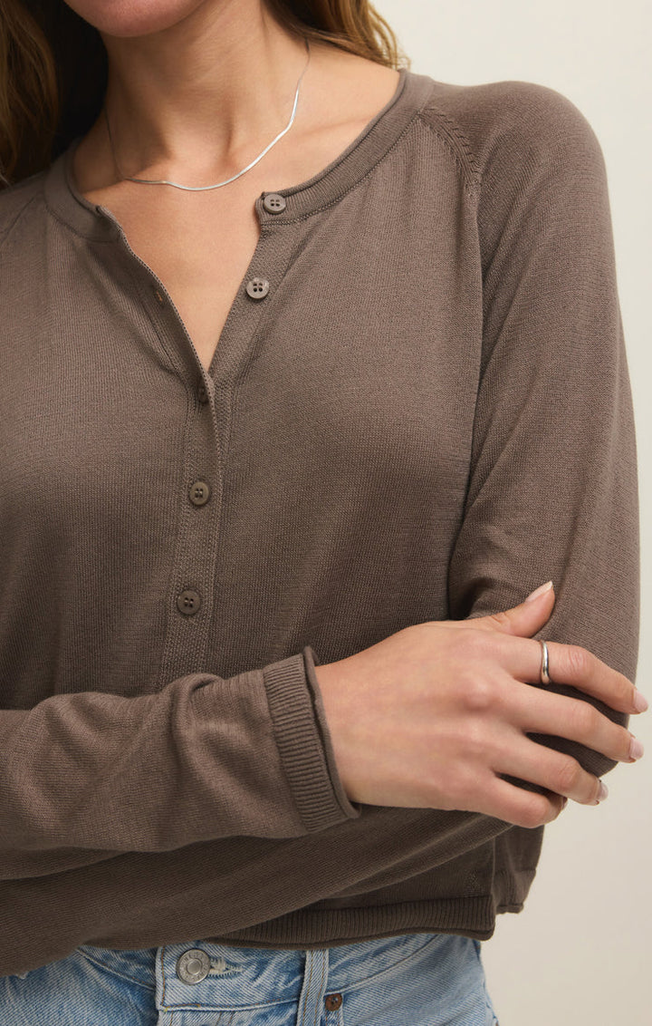 A woman in the Zertz THE PERFECT LAYER CARDIGAN in Perfectly Taupe (ZW261179) crosses her arms, wearing light blue jeans, a thin silver necklace, and a silver ring. Her head is partially out of the frame.
