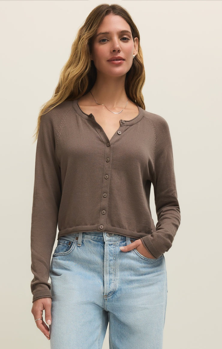 A woman with long, wavy hair wears the Zertz THE PERFECT LAYER CARDIGAN in Perfectly Taupe (ZW261179) and light blue high-waisted jeans, standing with one hand in her pocket against a plain light background.