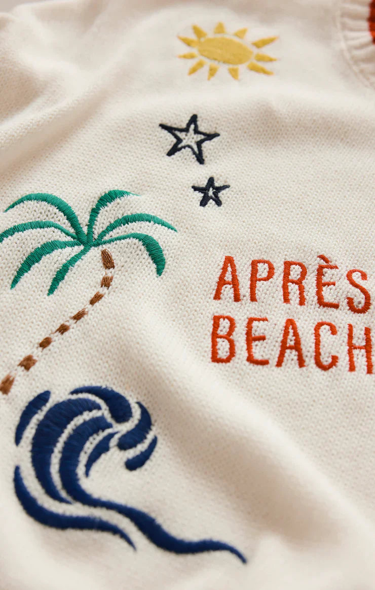 The SEAS THE DAY SIENNA SWEATER by Zertz features embroidered sun, stars, palm tree, ocean waves, and red "APRÈS BEACH" text on cotton fabric—the ideal summer layer.