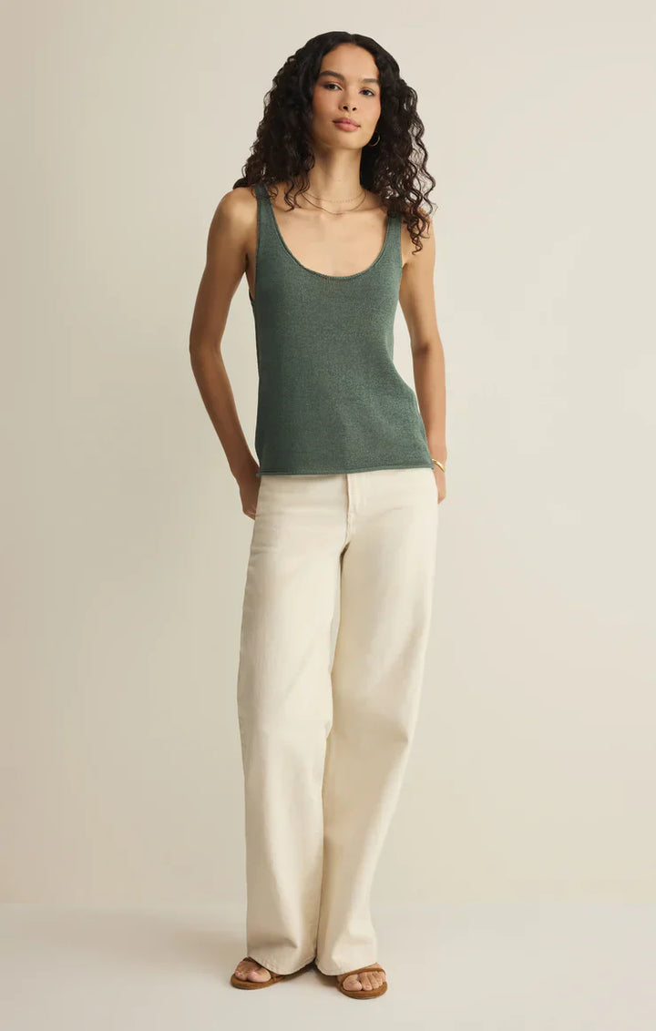 A person with long curly hair wears the Zertz PERCH SWEATER TANK in green, wide-leg cream pants, and brown sandals, standing against a plain light background with hands in their pockets.